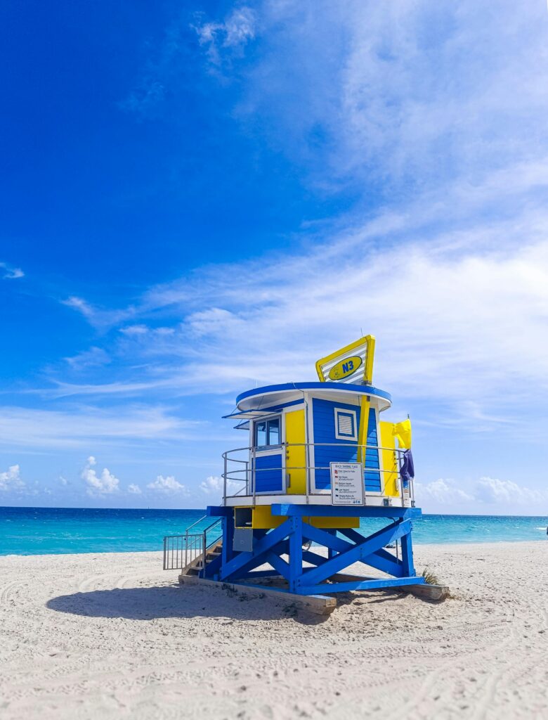 A lifeguard tower surrounded by white sand with a view of the beach's ocean in the background.